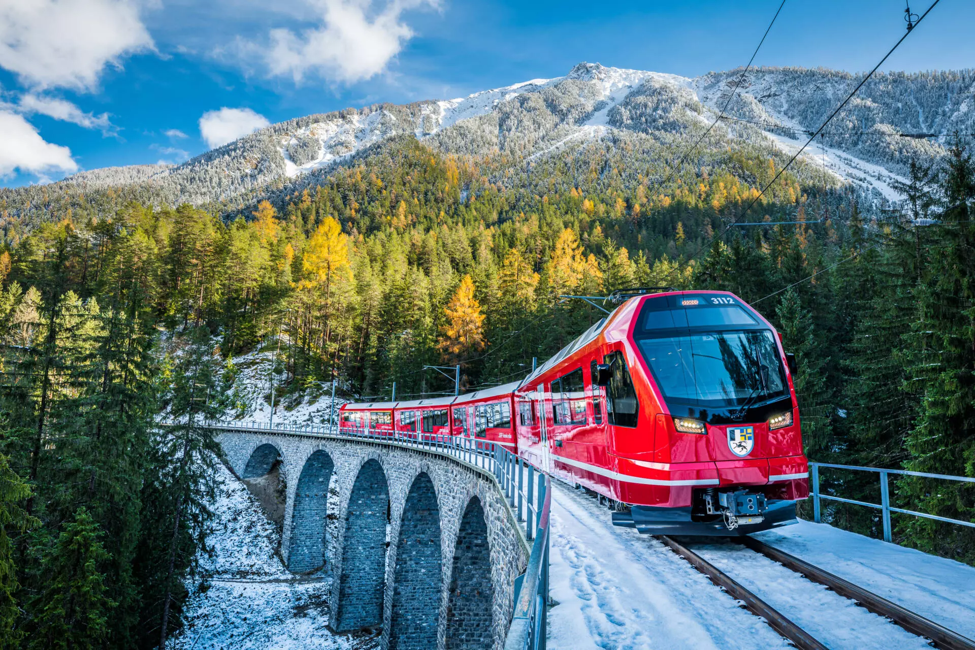 Roter Triebzug der Rhätischen Bahn auf einem Steinviadukt in verschneiter Berglandschaft